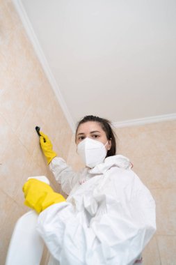Beyaz koruyucu elbiseli kadın fırça tutuyor ve konut ve ticari binalar için küf temizleme hizmetleri sunuyor..