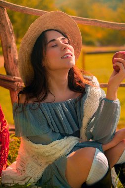 Bir kadın olgun kırmızı bir elma tutuyor, bir sonbahar parkında taze bir ısırığın tadını çıkarıyor, çiftlik elmalarının ve doğal ürünlerin tazeliğini vurguluyor..