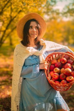 Elinde elma dolu bir sepet tutan genç bir kadın çiftçi meyve bahçelerinin, yetiştirilen ürünlerin ve elma yetiştirmenin cazibesini teşvik ediyor..
