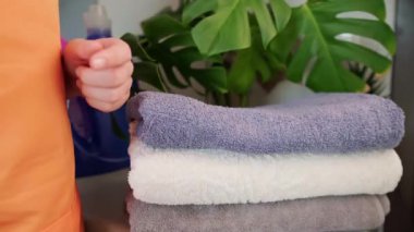 Kadın bir yığın temiz havluyu katlıyor, elini yumuşak ve taze kumaşın üzerinden nazikçe geçiriyor. Yüksek kalite 4k görüntü