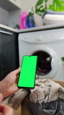 Ev işleri için mobil uygulamalar. Çamaşır ve tasarruflar için hatırlatmalar. Elinde yeşil ekranlı bir telefon tutan kadın. Yüksek kalite 4k görüntü