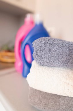 Çamaşır makinesine düzgünce yerleştirilmiş temiz havlular. Arka planda iki şişe çamaşır deterjanı var..