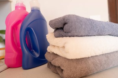 Çamaşır makinesinin üzerine katlanmış temiz çamaşırlar, arka planda deterjan ve yumuşatıcı ile taze çamaşır kokusu..