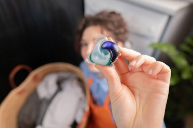 Woman holds a laundry capsule in hand, preparing to wash clothes, with focus on removing tough stains. clipart