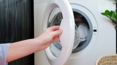 Bir kadın çamaşır makinesini temiz giysilerle açar, nemli giysileri çamaşır varilinden çıkarır. Yüksek kalite 4k görüntü