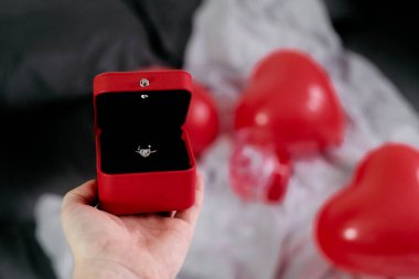 Evlilik yüzüğü kutusu, arka planda kalp şeklinde balonlar olan birinin avucunda durur. Sevgililer Günü 'nü kutlarlar..