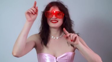 Fotoğraf makinesi için dans eden pembe elbiseli ve kırmızı gözlüklü bir kızın portresi, Sevgililer Günü partisini mutlu bir şekilde kutluyor. Yüksek kalite 4k görüntü