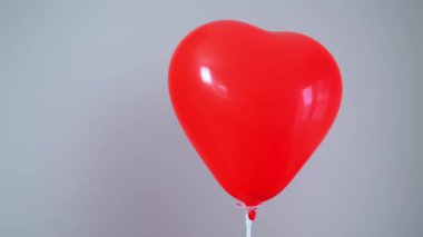 Kırmızı kalp şeklinde bir balon gri bir arka planda ileri geri sallanıyor, Sevgililer Günü 'nü simgeliyor, mesaj için yeri var. Yüksek kalite 4k görüntü