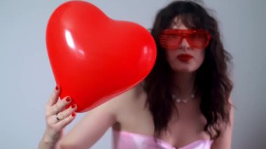 Sevgililer Günü partisinde elinde kalp şeklinde bir balon ve ellerinde kutlamanın sembolüyle dans eden mutlu bir kadın. Yüksek kalite 4k görüntü