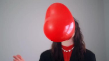 Siyah ceketli ve kırmızı bluzlu bir kız, sevgililer gününü kutlamak için kırmızı kalp şeklinde bir balonla oynuyor. Yüksek kalite 4k görüntü