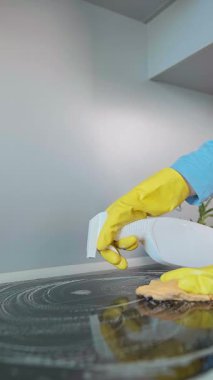 Önlüklü bir kadın mutfak sobasını temizlik ürünleriyle temizliyor. Dezenfektanlarla ıslak temizleme yemek pişirdikten sonra kalan bakterileri öldürür. Yüksek kalite 4k görüntü