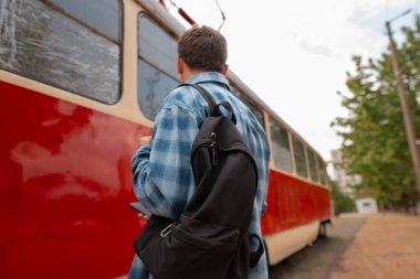 Sırt çantalı yalnız gezgin, sırtı trene dönük duruyor, tren istasyona varırken onu izliyor..