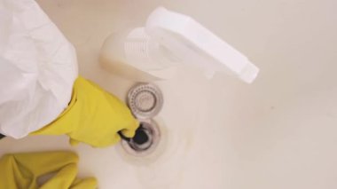 Koruyucu giysili ve lastik eldivenli bir kadın banyo giderini sünger ve temizlik kimyasallarıyla temizliyor. Yüksek kalite 4k görüntü