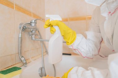 Koruyucu giysili kadın ve eldivenler dikkatlice musluğu temizliyor ve sünger ve temizlik çözeltileriyle karıştırıyor..