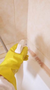 Koruyucu giysili kadın banyoyu temizliyor, küveti ovuyor ve lekesiz sonuç elde etmek için güçlü temizlik ürünleriyle batıyor. Yüksek kalite 4k görüntü