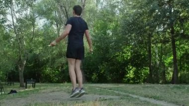 Sağlıklı kalmak için basit ama etkili bir yöntem: Yeşil bir parkta atlama halatıyla atlayan bir adam. Yüksek kalite 4k görüntü
