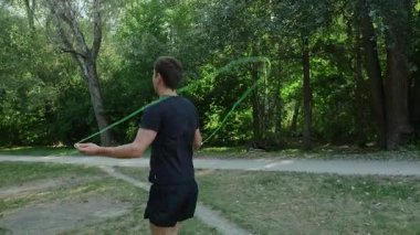 Spor kıyafetleri içinde bir adam parkta ip atlama egzersizlerinden hoşlanır. Her atlayışında zindeliğini ve sağlığını korur. Yüksek kalite 4k görüntü