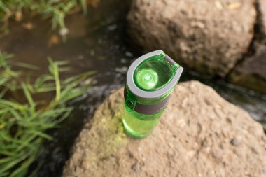 Doğa ve sağlık: nehir kenarındaki yeşil su şişesi sadece böbrek sağlığı için saf su içme ihtiyacını simgeler.