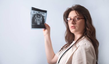 Kadın dişçi, tedavi ihtiyacını belirlemek için hastanın röntgenini dikkatlice inceler..