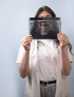 Kadın dişçi, potansiyel diş patolojisini elemek için hastanın röntgenini dikkatlice inceler..