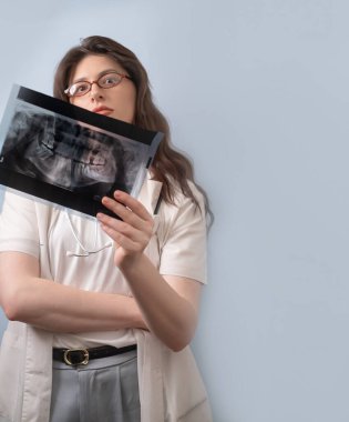 Kadın dişçi röntgen görüntüsü tutuyor ve hastanın dişleri için tedavi stratejisini belirliyor..