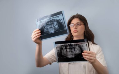 Kadın dişçi, değişimleri tespit etmek ve hasta için doğru bir teşhis koymak için iki röntgeni analiz eder..