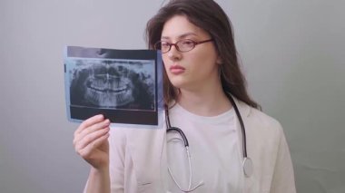 Beyaz önlüklü bir dişçi X-ray görüntüsü tutuyor ve olası diş patolojilerini dikkatle inceliyor. Yüksek kalite 4k görüntü