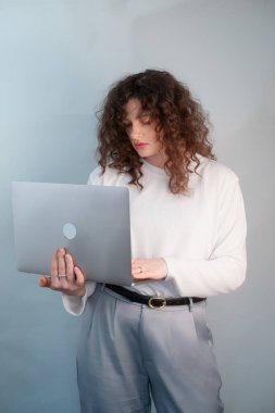 Beyaz kazaklı ve gri pantolonlu odaklanmış kız öğrenci ellerinde dizüstü bilgisayar ve kafasında kablosuz kulaklıkla online sınava giriyor..