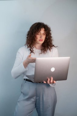 Öğrenci beyaz kazak ve gri pantolonla internetten öğrenmeye hazır, dizüstü bilgisayar ve kablosuz kulaklık tutuyor, modern eğitimi sembolize ediyor.