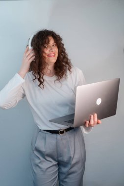 Beyaz kazaklı ve gri pantolonlu genç kız öğrenci internet üzerinden üniversite dersi alıyor, kablosuz kulaklıklı ders çalışmalara odaklanıyor..