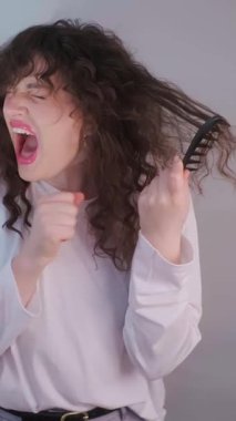 Kıvırcık saçlı herkes bilir ki acı çeken kadın, gerçek hayattaki saç mücadelede birbirine dolanmış kilitleri tararken yüzünü buruşturur. Yüksek kalite 4k görüntü