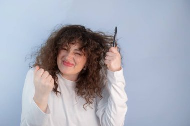 Kıvırcık saçlı kadın sabah düğümleriyle savaşıyor umutsuzca saçını çözmeye çalışıyor hayal kırıklığını ve gerçek hayattaki güzellik rutinini gösteriyor.