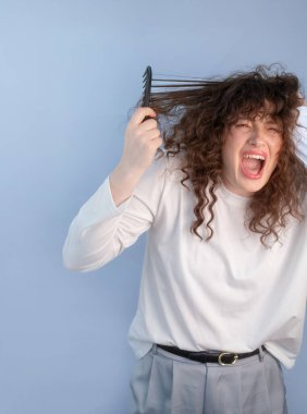 Hüsrana uğramış kıvırcık saçlı kadın evde karışık saçlarını taramaya çalışırken acı içinde çığlık atıyor..