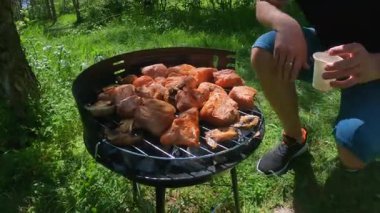 Kırsal kesimde ya da kamp alanında barbekü yapan adam, yanında durup dışarıda kokteylinin tadını çıkarırken et ızgara yapıyor. Yüksek kalite 4k görüntü