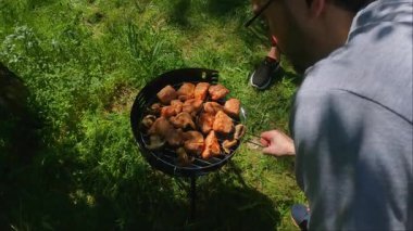 İnsan, doğanın, taze hava ve yeşillik ile çevrili lezzetli bifteklerle dolu ızgarayı açık havada pişirmekten zevk alır. Yüksek kalite 4k görüntü