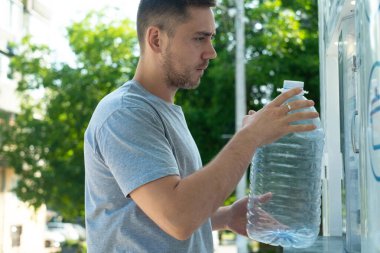 Adam, sürdürülebilir tüketim ve ekolojik bilinçli yaşam tarzını gösteren tekrar kullanılabilir bir şişeyi dolduran bir su otomatının yanında duruyor.