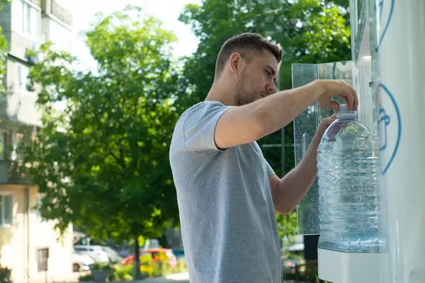Plastik atık olmadan temiz içme suyu kullanan adam, sürdürülebilir yaşam tarzını destekleyen yeniden kullanılabilir şişeli otomat kullanıyor.
