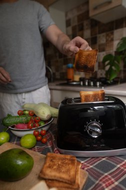Sabah rutini yapan adam, basit ev yapımı kahvaltı hazırlamak için avokado ve sebzeli gevrek tost yapar.