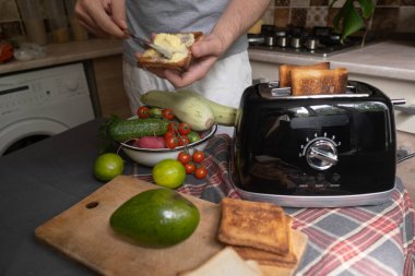 Sağlıklı yaşam tarzı adamı avokado tostu hazırlamak için ekmek kızartıyor. Güne basit ev yapımı yemeklerle başlıyor.