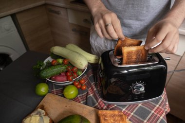 Adam ekmeği tost makinesine koyar ve güne taze bir başlangıç için avokado ve sebzelerle sağlıklı bir kahvaltı hazırlar.