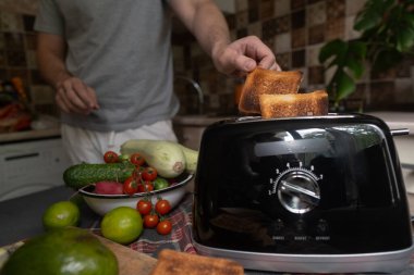 İnsan, sebze ve sebzelerle sağlıklı bir kahvaltı hazırlamak için tost makinesi kullanır. Evde taze malzemelerle basit bir sabah yemeği.