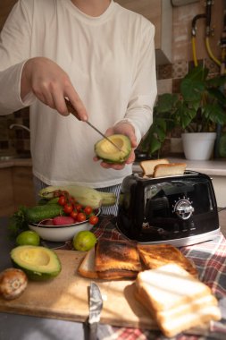 Avokado tostu hazırlayan kadın evde hızlı ve besleyici bir sabah yemeği için tost makinesi kullanarak sağlıklı bir kahvaltı hazırlıyor.