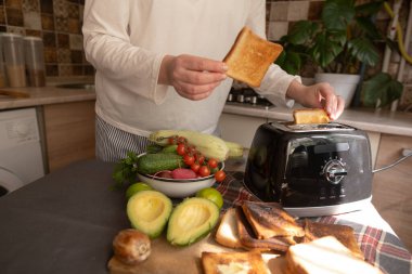 Evde genç bir kadın tost makinesini kızarmış ekmek ve günlük mutfak rutiniyle kahvaltı hazırlamak için kullanır..