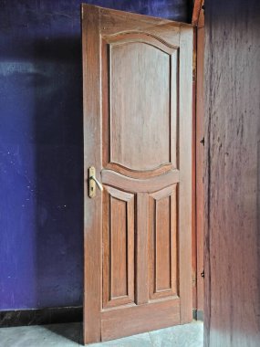 Klasik paneli olan kısmen açık ahşap bir kapı koyu mor bir duvar ve gri döşemeli döşeme..