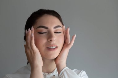 Genç bir kadın rahatlamak için yüzüne masaj yapıyor. Düşüncelere dalmış gözleri kapalı bir kadın portresi.