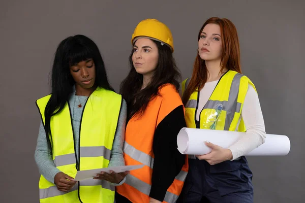 stock image Three models of different ethnicities posing, dressed as construction workers. Reflective vests, hard hats and rolled up project.