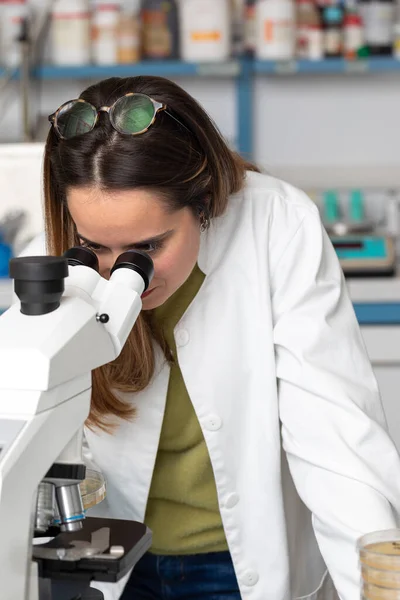 Young scientist woman under a microscope in a scientific laboratory. Research concept for rare diseases and scientific excellence. Biologist during a lab test with reagents in the background