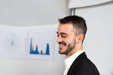 Young newly hired entrepreneur smiling satisfied with his success. Finance graphs on the white background and large advertising copy space