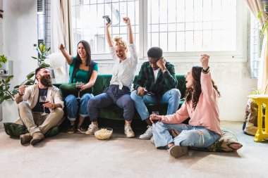 Çok ırklı bir grup genç kız ve erkek bilgisayar oyunlarını kazandıktan sonra tezahürat yapıyor. Arkadaşlarla keyifli bir günde kanepede sakin bir ortam..