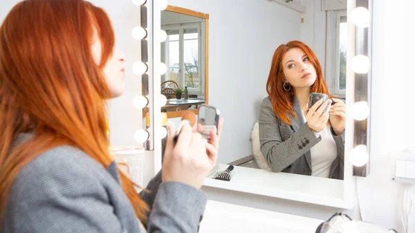 Businesswoman with elegant clothes doing her make up in front of the mirror before going to work. Female empowerment concept